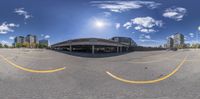 a parking lot with parked cars under a cloudy blue sky with a white sun behind it