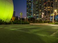 empty parking lot with buildings in the background and green lighting from street lamps at dusk