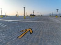 a sign pointing left at the parking lot of an airport runway with lots of parking spaces