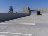 an empty parking lot with no grass or building to the side and blue water tower in the distance