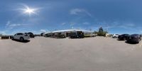 several cars sit in a parking lot with a stadium and blue sky in the background