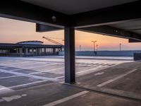 a parking lot near the ocean at dusk with a building in the back ground at the center