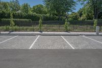 a car park with a fence, trees and paved street surface with parking spaces and white lines