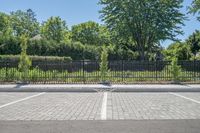 a car park with a fence, trees and paved street surface with parking spaces and white lines