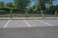 a car park with a fence, trees and paved street surface with parking spaces and white lines