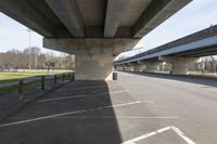 a parking lot under an overpass, in the shade of a sunny day and sunlight from a nearby building