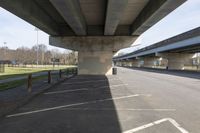 a parking lot under an overpass, in the shade of a sunny day and sunlight from a nearby building