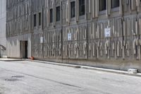 two parking meters on the side of a large building next to a street with parking spaces and several signs