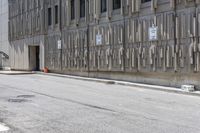 two parking meters on the side of a large building next to a street with parking spaces and several signs