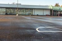 an empty parking lot near a supermarket building that has a basketball hoop painted on the concrete