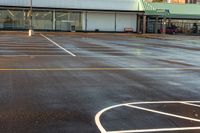 an empty parking lot near a supermarket building that has a basketball hoop painted on the concrete