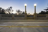 the empty paved bridge has illuminated street lamps lit up at night and people walking over it