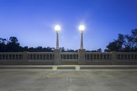 the empty paved bridge has illuminated street lamps lit up at night and people walking over it