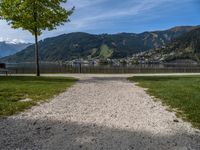 the path leads up to a park by the water, and is surrounded by grassy area with mountains in the background