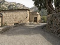 an image of the path to a stone house in the mountainside with trees and rocks around it