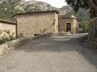 an image of the path to a stone house in the mountainside with trees and rocks around it