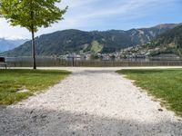 a pathway is near the water with a bench in the middle of it and mountains behind