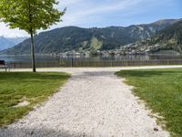 a pathway is near the water with a bench in the middle of it and mountains behind