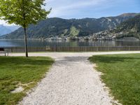 a pathway is near the water with a bench in the middle of it and mountains behind