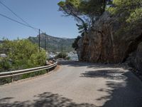 a paved country road near a mountain side with some trees and hills behind it, near a large body of water