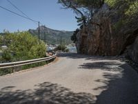 a paved country road near a mountain side with some trees and hills behind it, near a large body of water