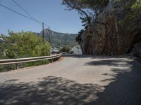 a paved country road near a mountain side with some trees and hills behind it, near a large body of water