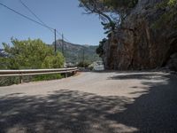 a paved country road near a mountain side with some trees and hills behind it, near a large body of water