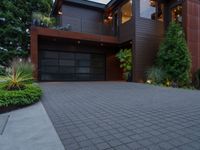 the driveway is paved with pavers between a brick and tree with plants surrounding it