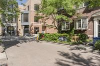 a paved driveway in front of a building with a tree in the front ground, and an open space between the buildings