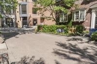 a paved driveway in front of a building with a tree in the front ground, and an open space between the buildings