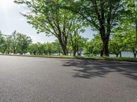 a paved parking lot is surrounded by lush trees on a sunny day along a river