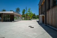 a paved concrete plaza with benches and trees in front of a building with two doors