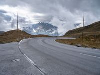 a paved road with a mountain in the background with clouds overhead and mountains in the distance