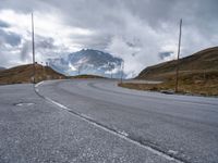 a paved road with a mountain in the background with clouds overhead and mountains in the distance