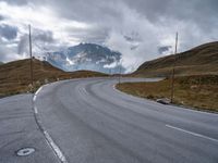 a paved road with a mountain in the background with clouds overhead and mountains in the distance