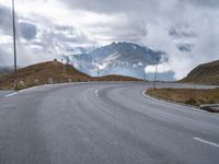 a paved road with a mountain in the background with clouds overhead and mountains in the distance