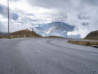 a paved road with a mountain in the background with clouds overhead and mountains in the distance