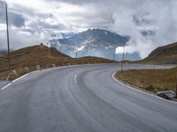 a paved road with a mountain in the background with clouds overhead and mountains in the distance