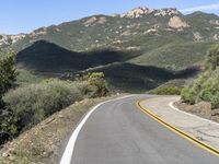 a lone motorcycle on a paved road in the mountains by a mountain range with trees