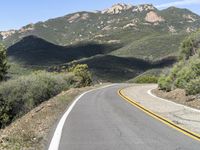 a lone motorcycle on a paved road in the mountains by a mountain range with trees