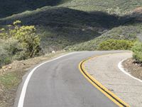 a lone motorcycle on a paved road in the mountains by a mountain range with trees