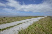 a paved road on a dry grass covered plain next to a body of water with grass growing up side