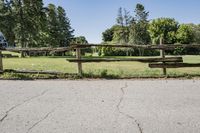 the road is paved and has grass behind it, with an old gate that extends the yard to the meadow