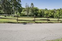 the road is paved and has grass behind it, with an old gate that extends the yard to the meadow