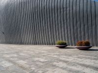 two large planters on a brick sidewalk in front of a wall with metallic siding