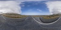 a wide lens view of a paved road and sky in the background by some clouds