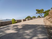 the paved road has a bench on it overlooking the sea and mountainside with trees