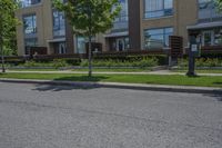 a paved road with two trees and lawns next to multi - unit building complex