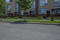 a paved road with two trees and lawns next to multi - unit building complex