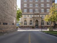 the paved street by the brick building has no traffic on it as well as trees